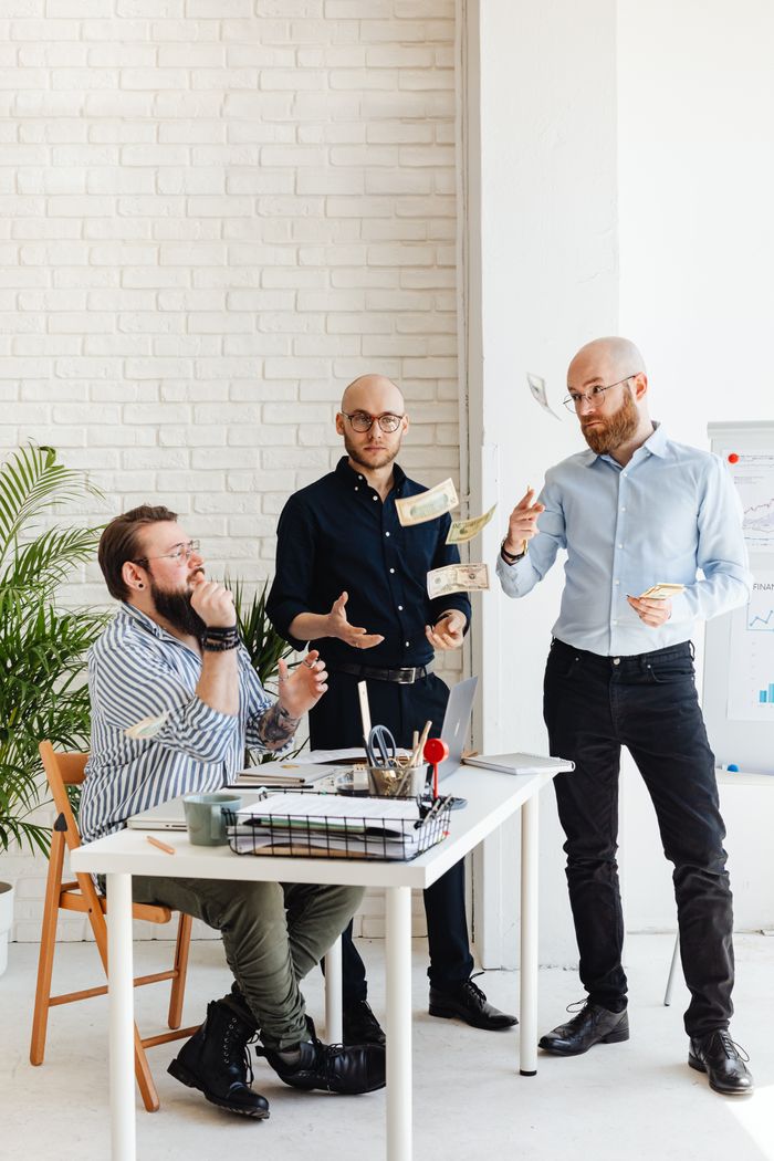 Crafting Captivating Headlines: Your awesome post title goes here Three men discuss business plans at an office desk, tossing papers and exchanging ideas.